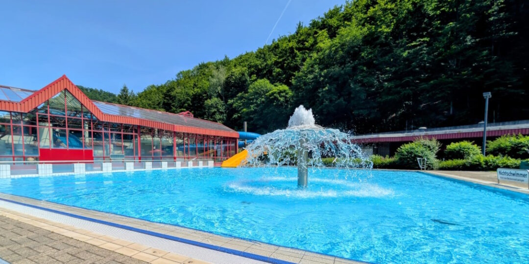 Außenbereich des Vitamar-Freibads im Harz mit Wasserpilz, Rutsche und umliegendem Wald bei sonnigem Sommerwetter.