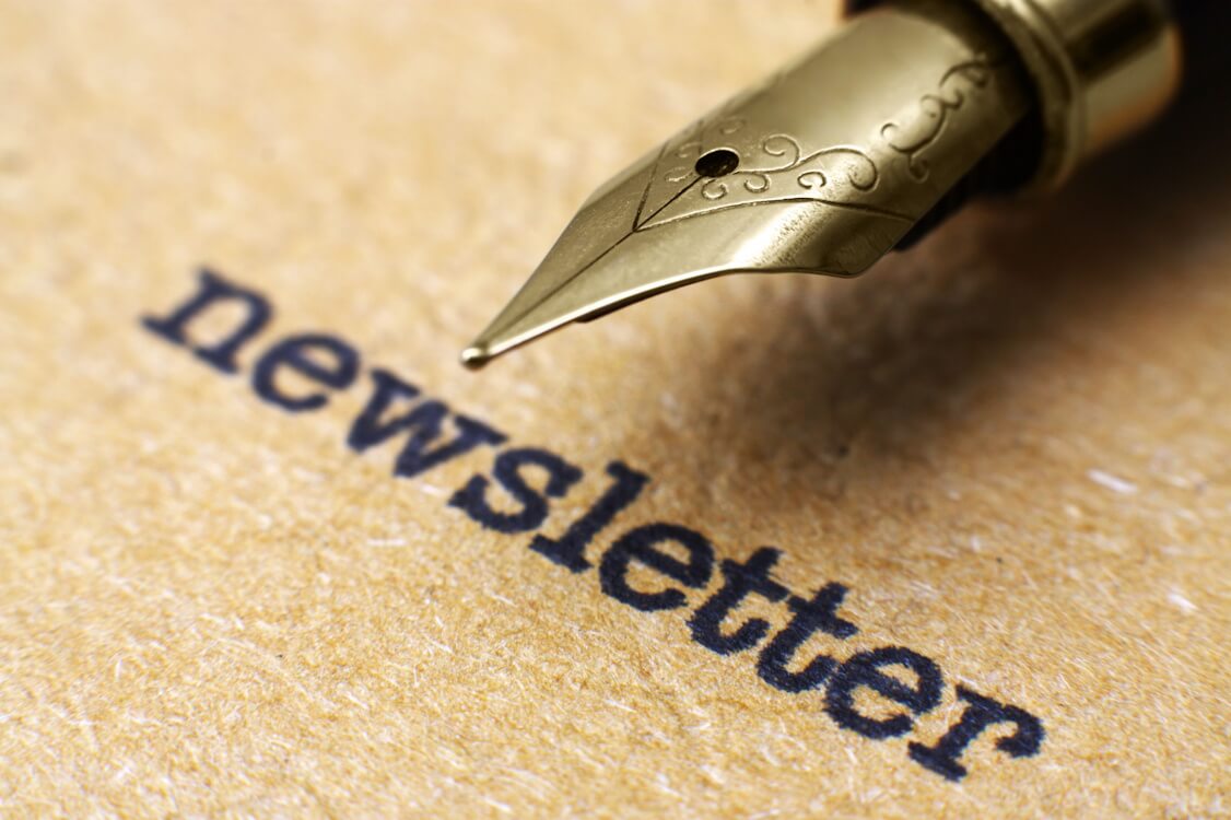 Nahaufnahme einer goldenen Feder mit der Aufschrift „Newsletter“ auf braunem Papier.